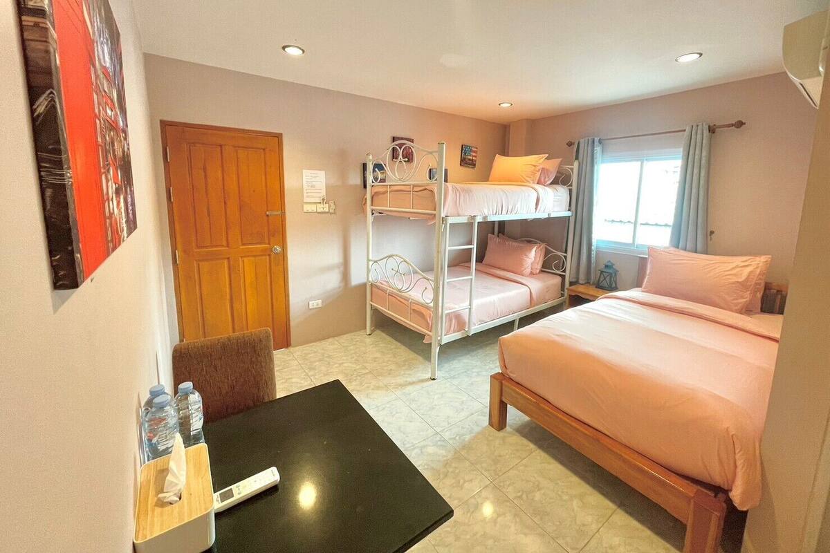 Een hotelkamer met stapelbedden, een bureau met stoel, een raam met gordijnen en een deur.