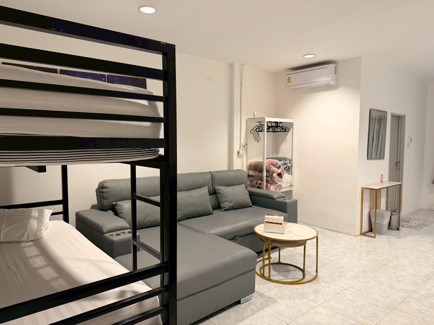 A modern room with a bunk bed, grey sofa, small round table, and an air conditioning unit.