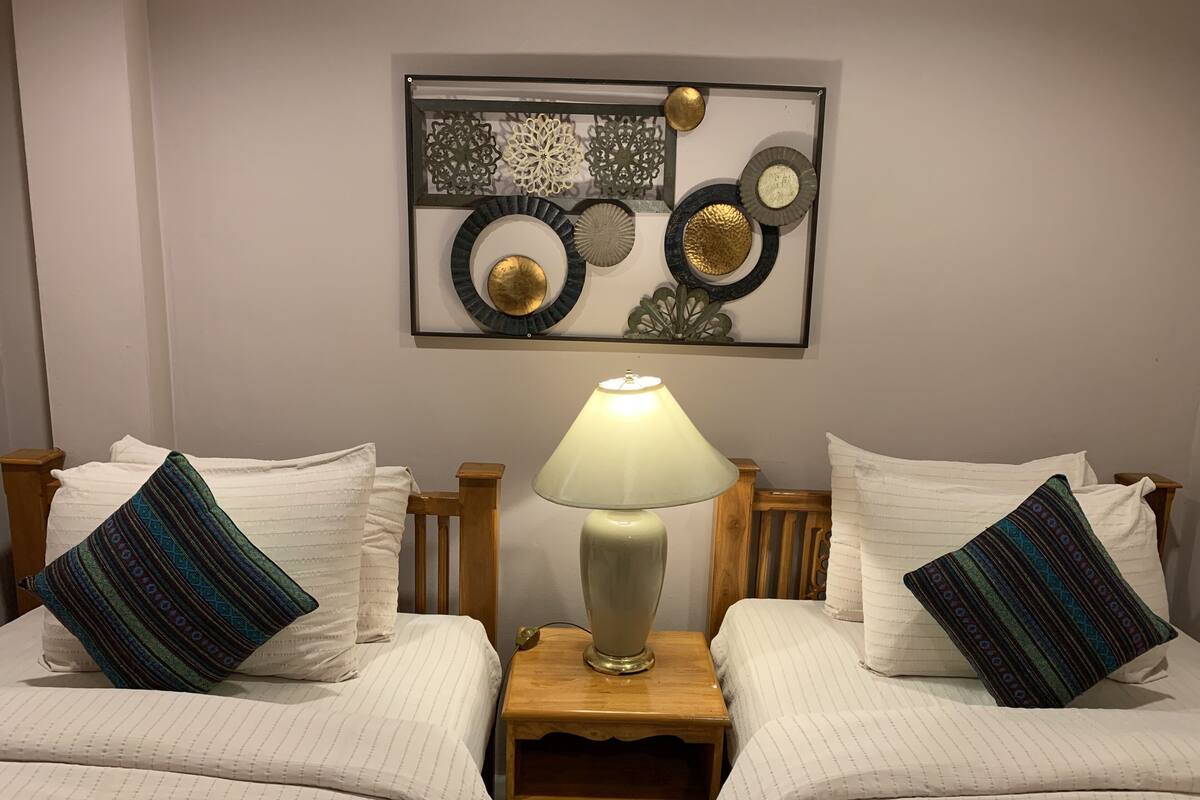 Een hotelkamer met twee bedden, een nachtkastje met een lamp en een decoratief object boven de bedden.