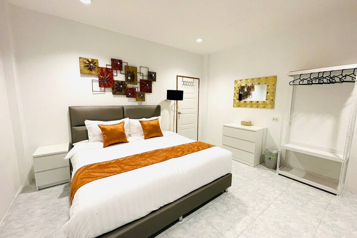 Een moderne slaapkamer met een groot bed, nachtkastje, dressoir, spiegel en een kledingkast.