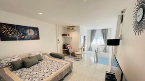Habitación de hotel moderna con una cama grande, un escritorio, una silla, un televisor y un balcón con cortinas.