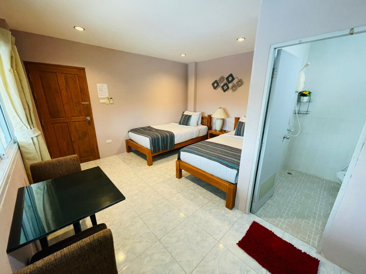 Ein Hotelzimmer mit zwei Betten, einem kleinen Tisch, einem Stuhl, einer Dusche und einem roten Teppich.