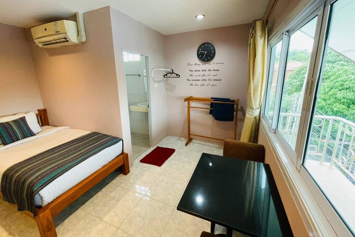 Hotelkamer met een bed, een klein tafeltje, een raam met uitzicht, een wandklok en een airconditioning.