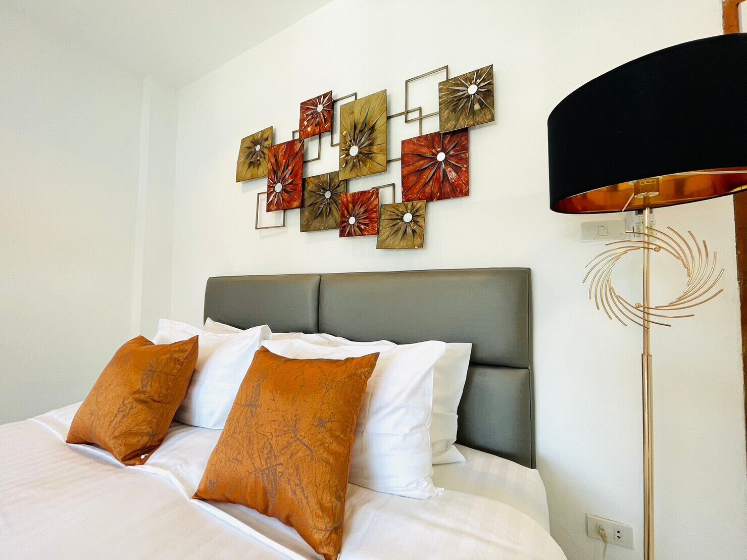A neatly made bed with white and brown pillows, a grey headboard, and a wall with abstract art pieces.