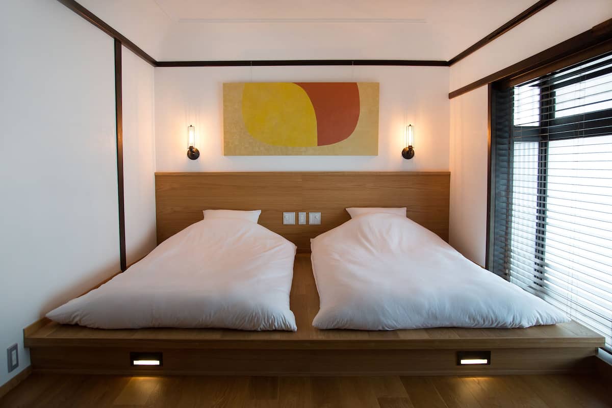 A modern bedroom with a wooden platform bed, two bedside lamps, and a large abstract painting on the wall.