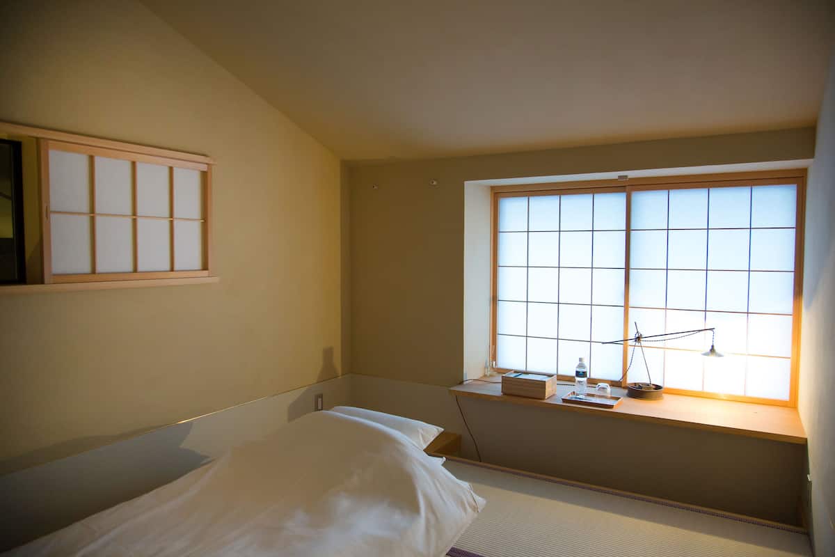 A bedroom with a bed, a window with a view, and a small table with a lamp.