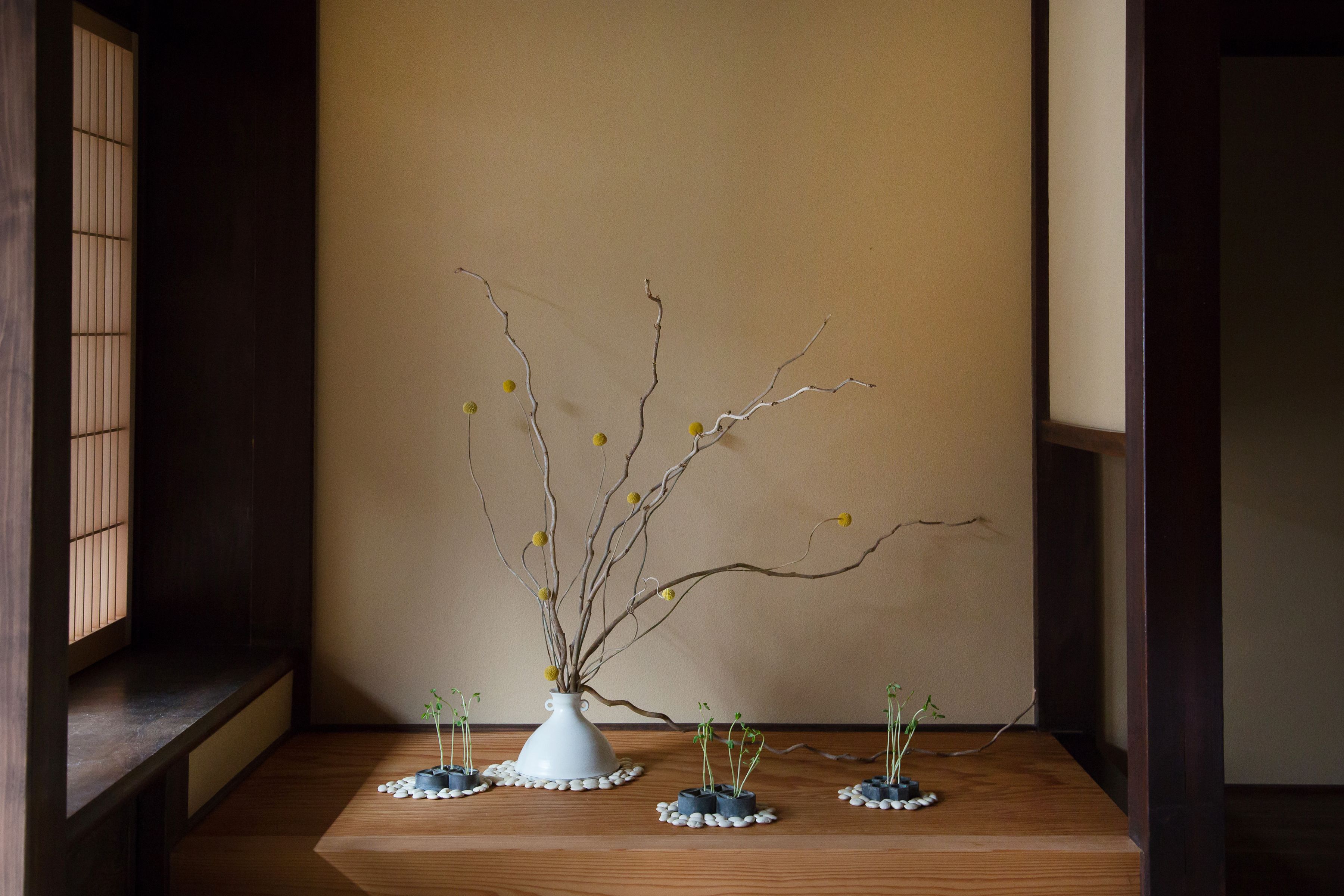 Una habitación tradicional japonesa con suelo de tatami, un celosía de papel shoji y una mesa de madera baja con un jarrón blanco y ramas.