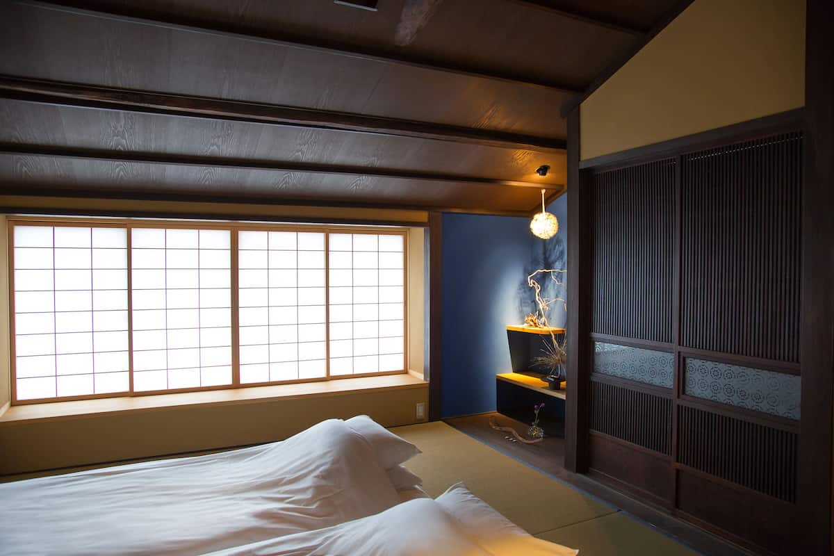 A traditional Japanese room with tatami flooring, a low bed, a shoji screen, and a hanging light fixture.