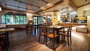 A spacious dining area with wooden flooring and tables, large windows offering a view of greenery, and a kitchen area with a coffee machine. - FangShug B&B (Fenglin)