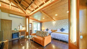 A room with a wooden ceiling, a bed with a floral wallpaper, a sofa, a small table, and a desk with a computer. - FangShug B&B (Fenglin)
