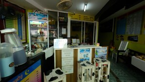 A small, brightly lit shop with a variety of items on display, including a refrigerated section with drinks and a sign for haircuts and other services. - RC Guesthouse (Ko Phi Phi)