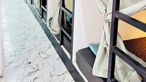 A row of bunk beds with curtains, a tiled floor, and a white wall. - RC Guesthouse (Ko Phi Phi)