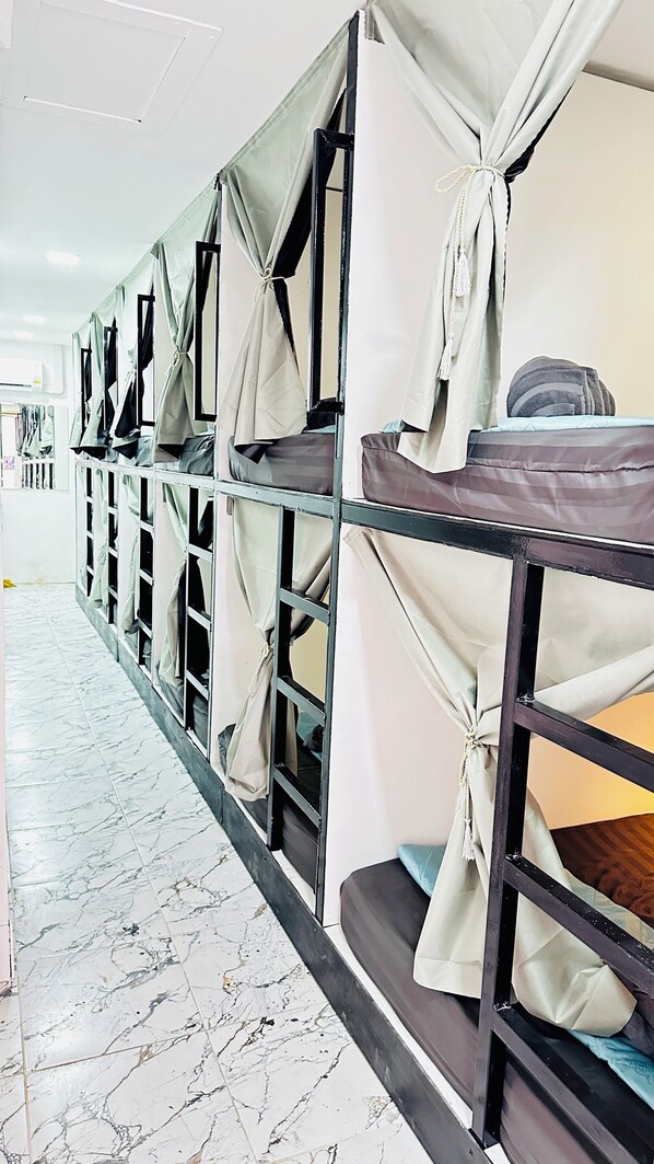 A row of bunk beds with curtains, a tiled floor, and a white wall.