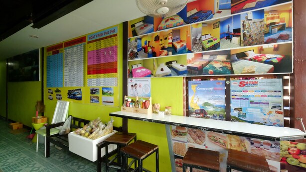 A room with a bed, a desk, a chair, and a fan. There are posters on the wall and a table with food items. - RC Guesthouse (Ko Phi Phi)