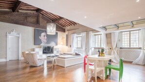 Amplia sala de estar con techo de madera, un sofá blanco, una mesa de comedor con sillas y un ventanal con cortinas.