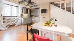 Una cocina moderna con encimera blanca, electrodomésticos de acero inoxidable y una zona de comedor con mesa y sillas blancas.