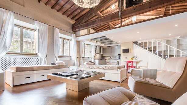 Un amplio salón con techo alto, vigas de madera, un sofá, una mesa de centro y una escalera que conduce a un nivel superior.