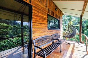Une terrasse en bois avec un banc et un fauteuil suspendu, donnant sur un jardin luxuriant.