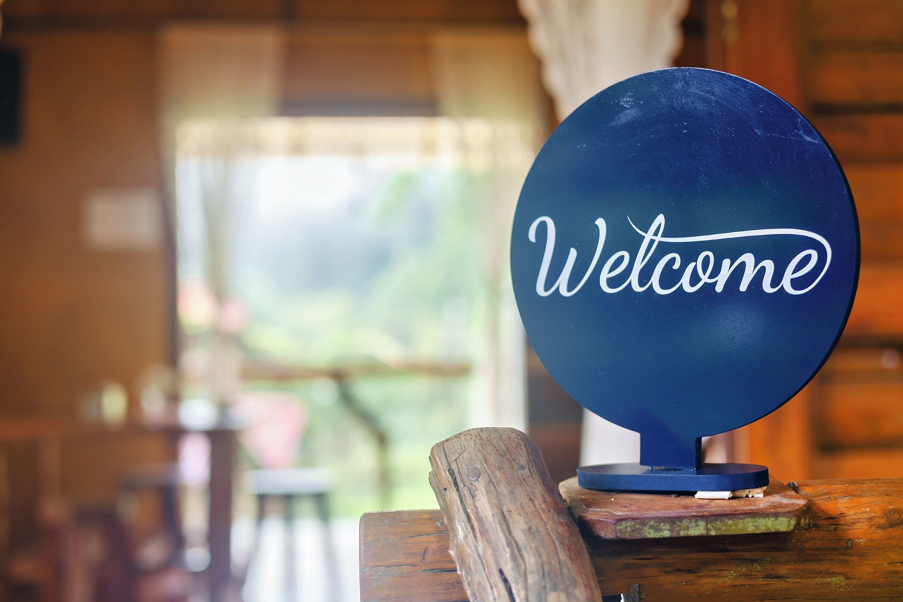 A blue sign with "Welcome" written on it, placed on a wooden stand.