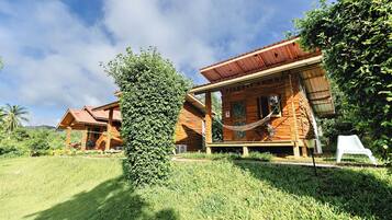A wooden cabin with a porch, surrounded by lush greenery and a clear sky.