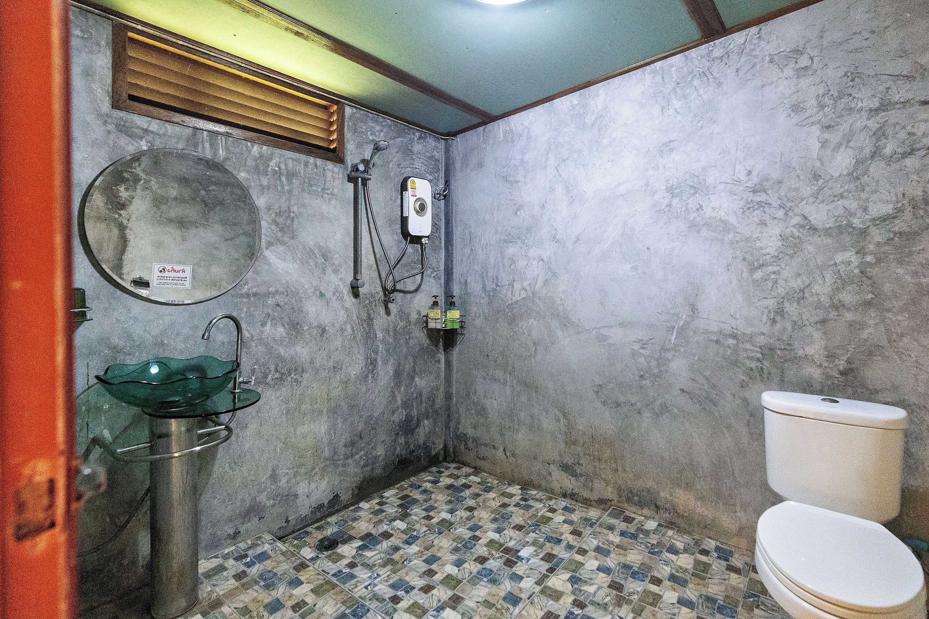 Un baño pequeño con inodoro, lavamanos de vidrio, espejo y cabina de ducha.