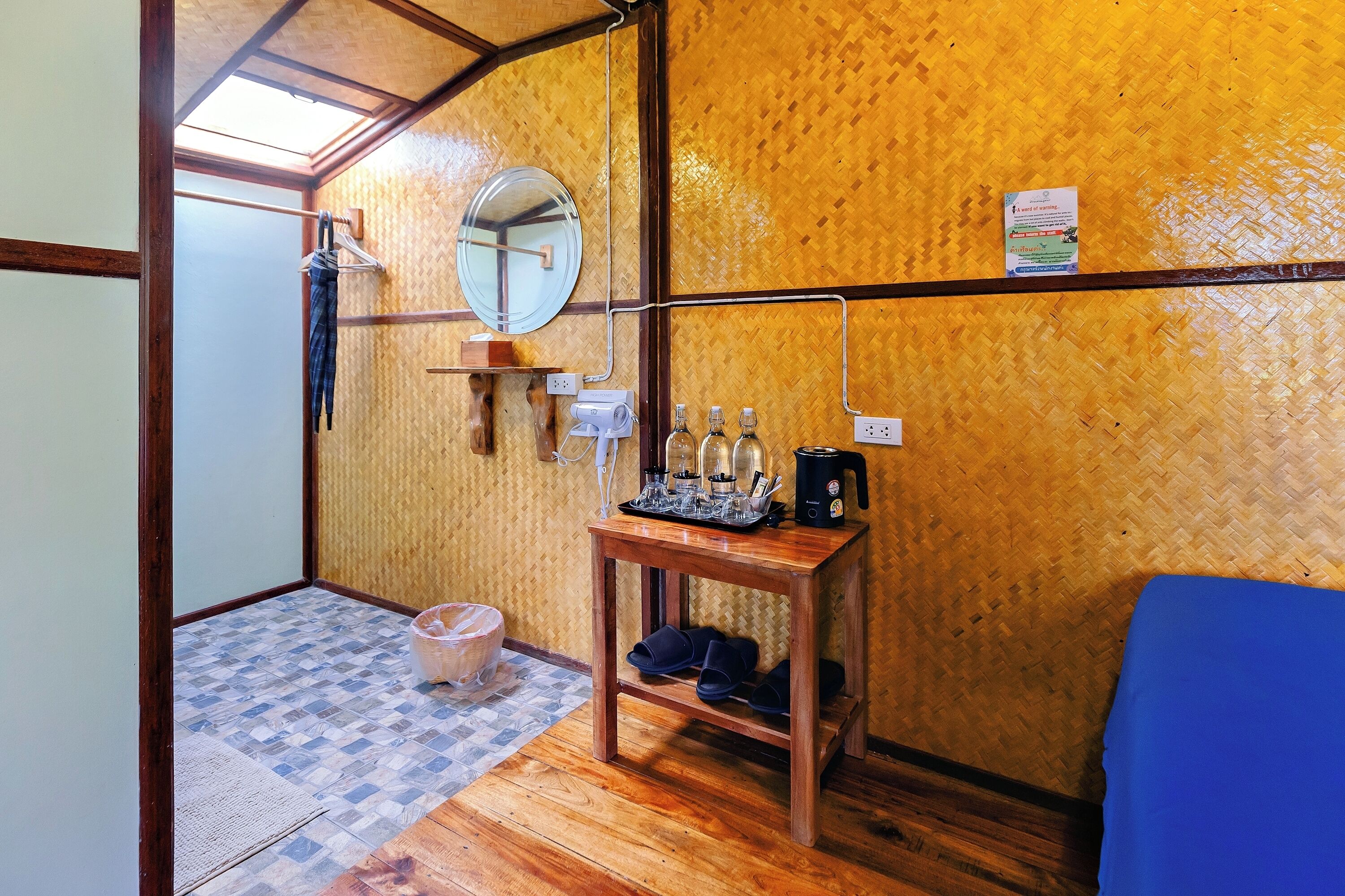 Una stanza compatta con pavimento in legno, un tavolino con un bollitore, uno specchio e un letto blu.