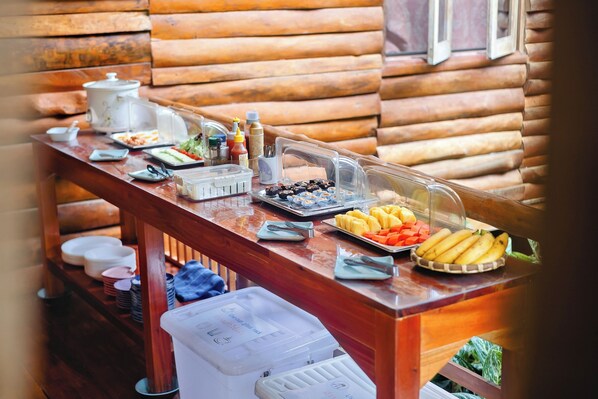 A buffet table with various food items and condiments, set against a wooden cabin backdrop. - Bansuanphutarn (Ban Ta Khun)