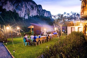 An outdoor dining area with tables and chairs, surrounded by lush greenery and a mountain backdrop. - Bansuanphutarn (Ban Ta Khun)