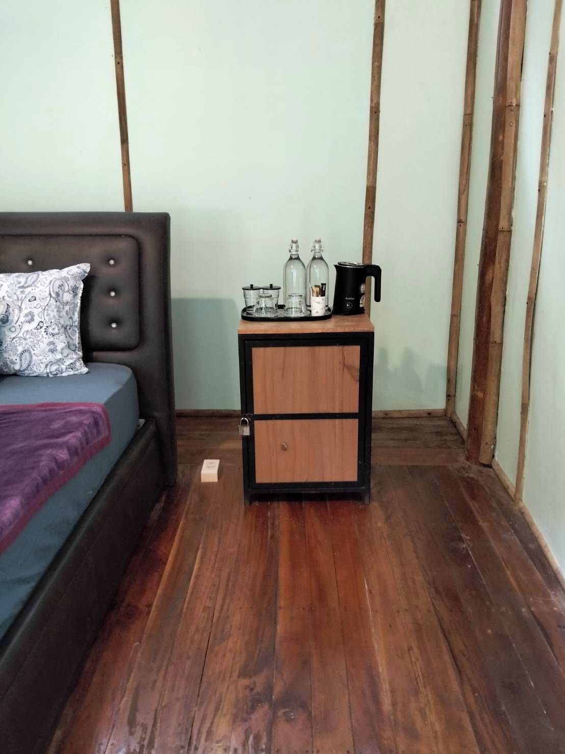 Un dormitorio con una cama, una mesita de noche con cafetera y un armario pequeño.