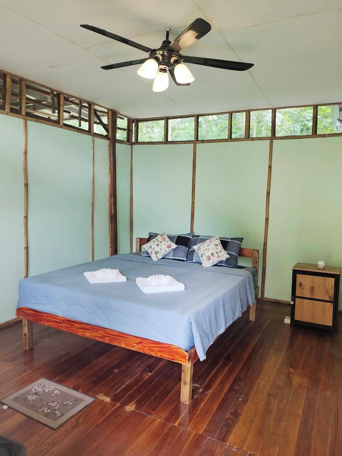 Quarto com cama, mesa de cabeceira, ventilador de teto e janela.