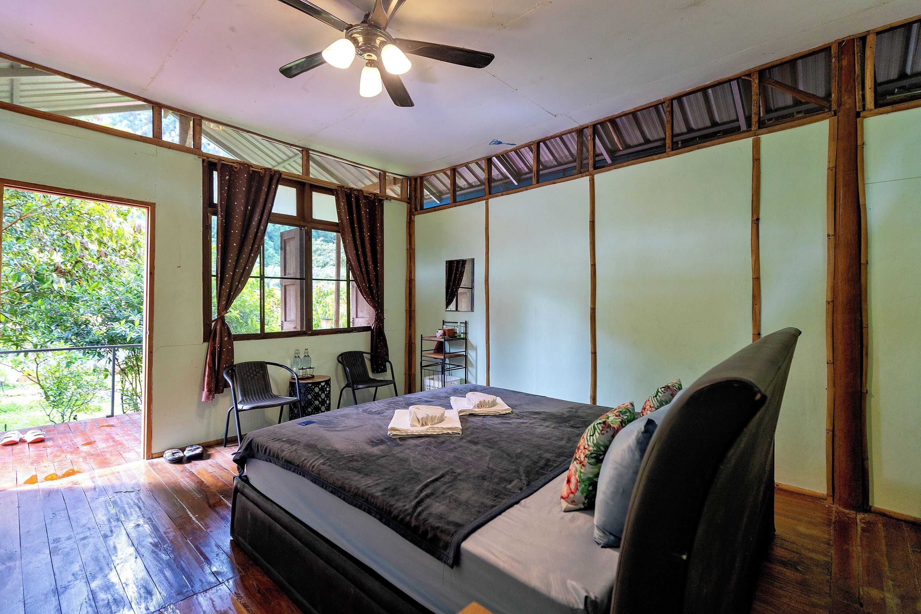 A bedroom with a bed, a ceiling fan, a window with curtains, a chair, and a small table.
