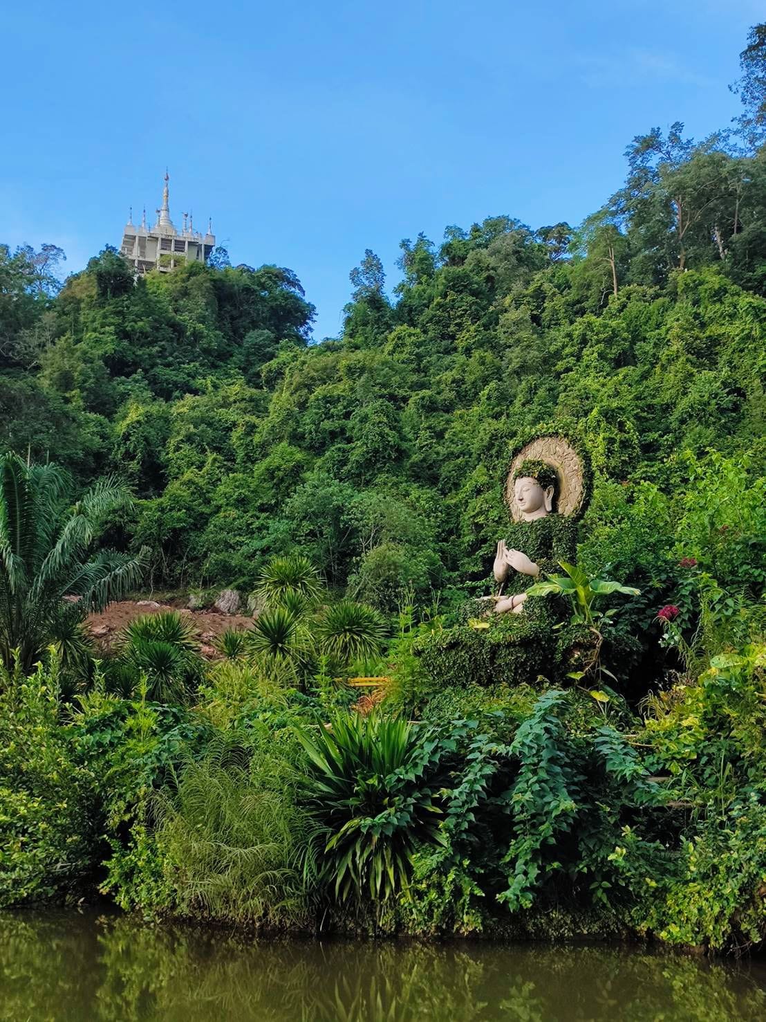 A large Buddha statue surrounded by lush greenery and a body of water.