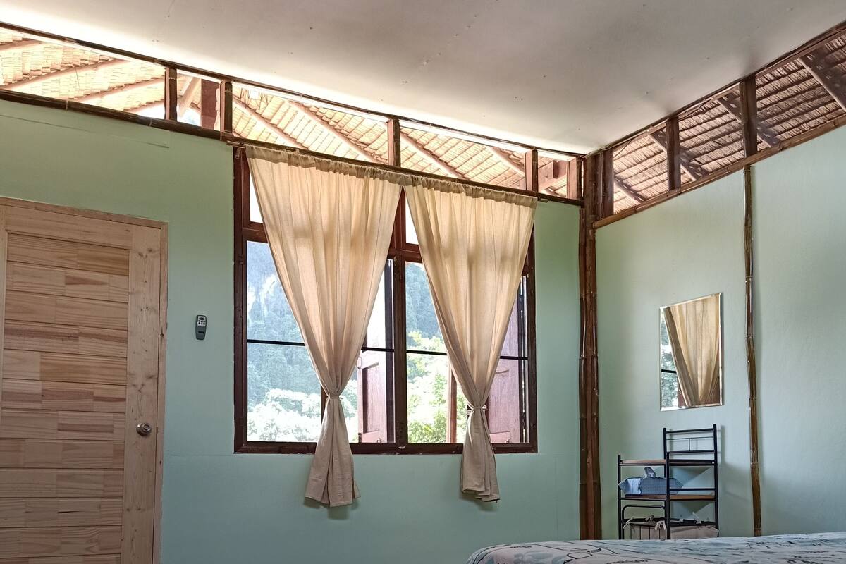 Una habitación con cama, suelo de madera, ventilador de techo y ventana con cortinas.
