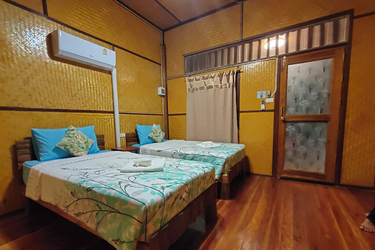 Habitación con dos camas, suelo de madera, aire acondicionado, ventana con cortinas y puerta con paneles de vidrio esmerilado.