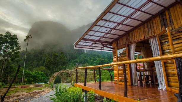 A wooden cabin with a covered deck and a view of a forested mountain range. - Bansuanphutarn (Ban Ta Khun)