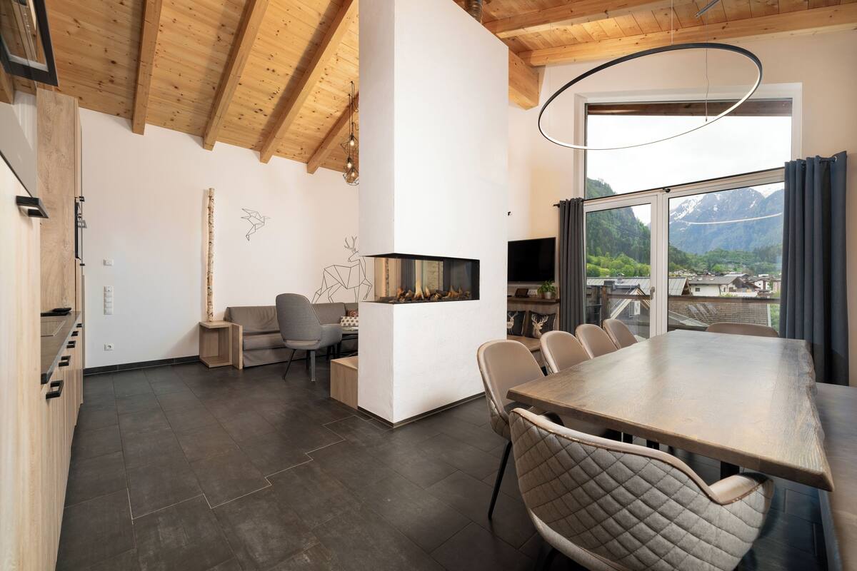 A modern dining area with a wooden table and chairs, a fireplace, and a large window with a mountain view.