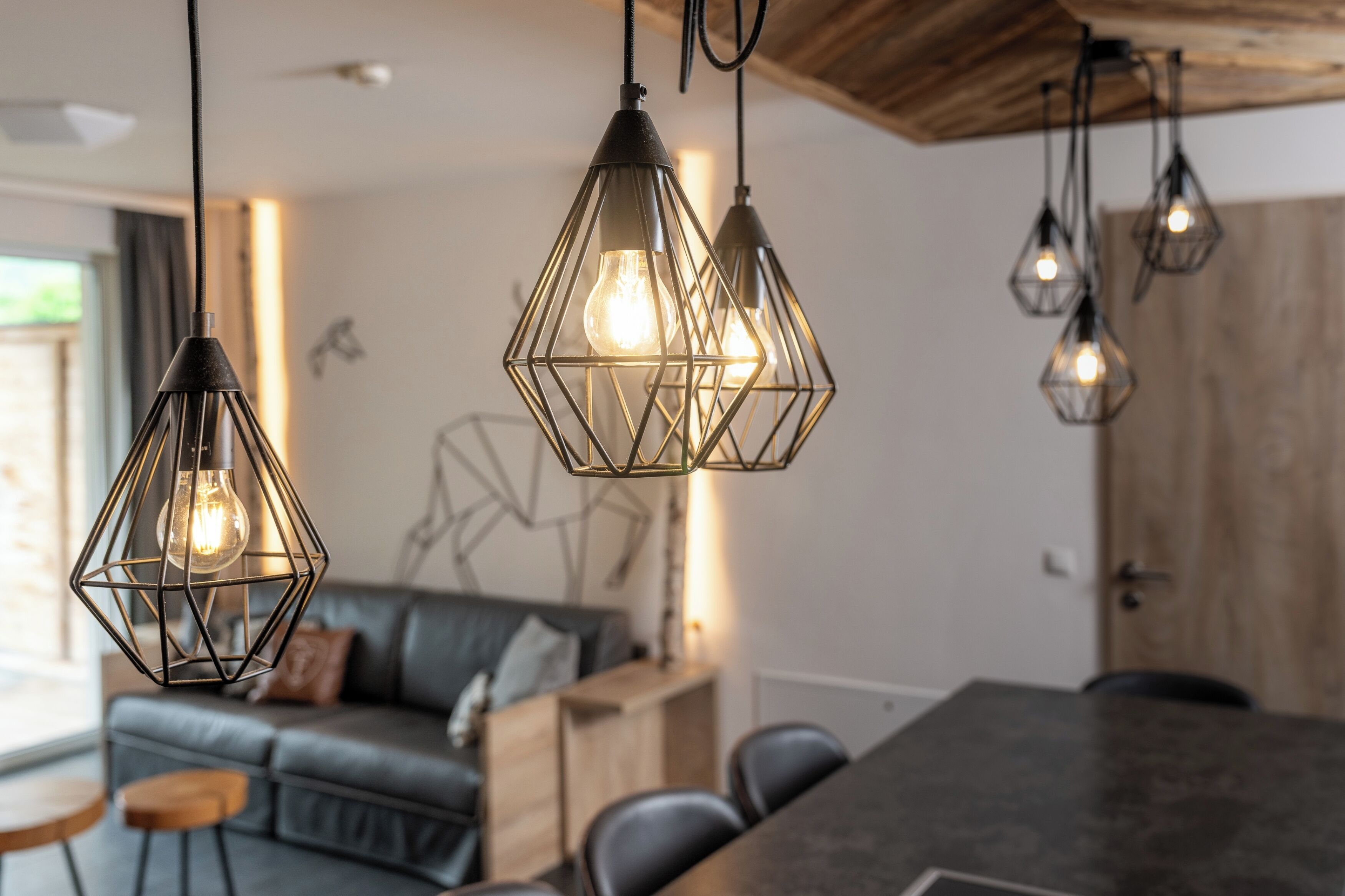 Un espace repas moderne avec une table en bois foncé et des chaises noires, un canapé en cuir avec des coussins et des œuvres d’art géométriques accrochées au mur.