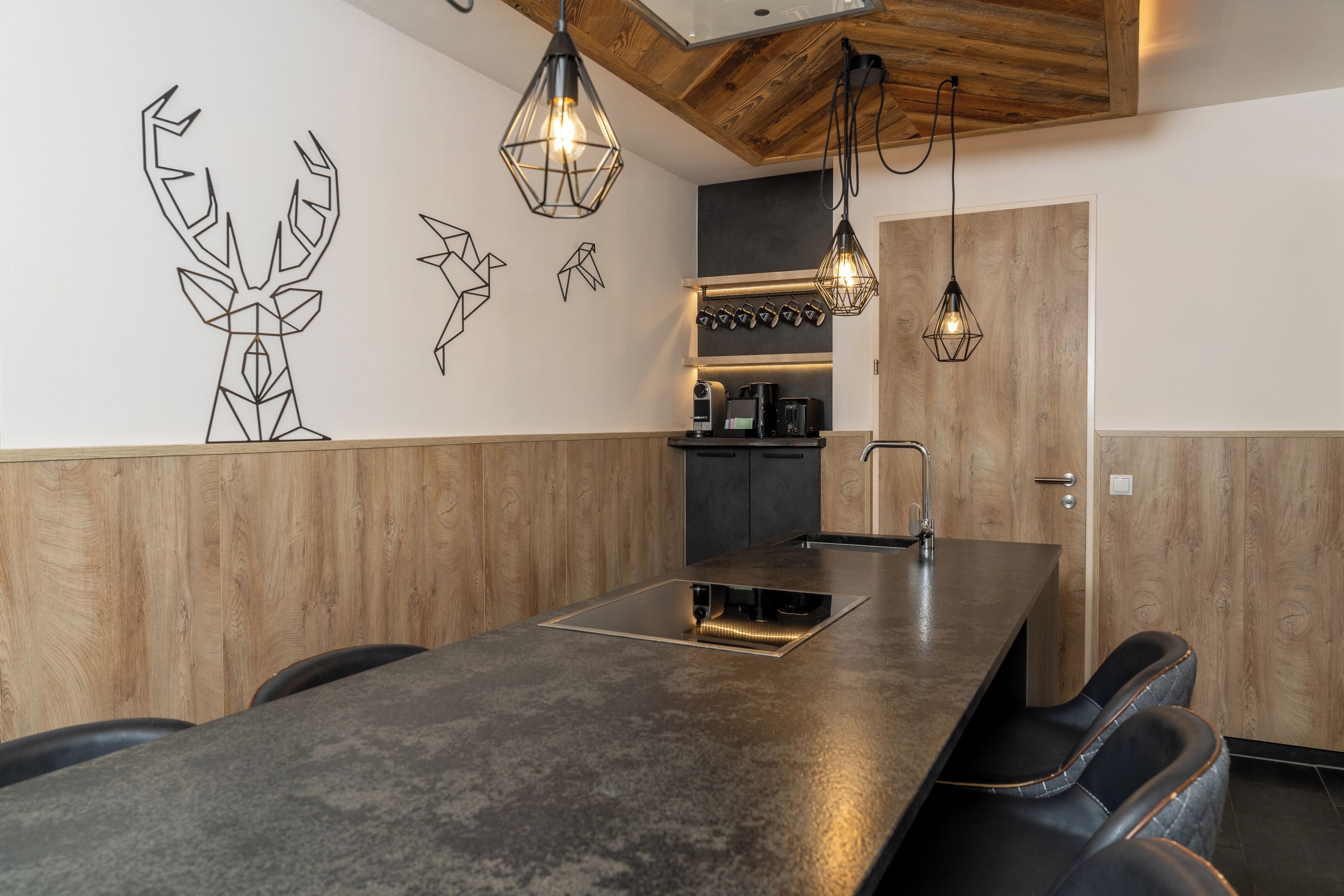 Una cocina moderna con un revestimiento de madera, una isla integrada, iluminación colgante y una cafetera.