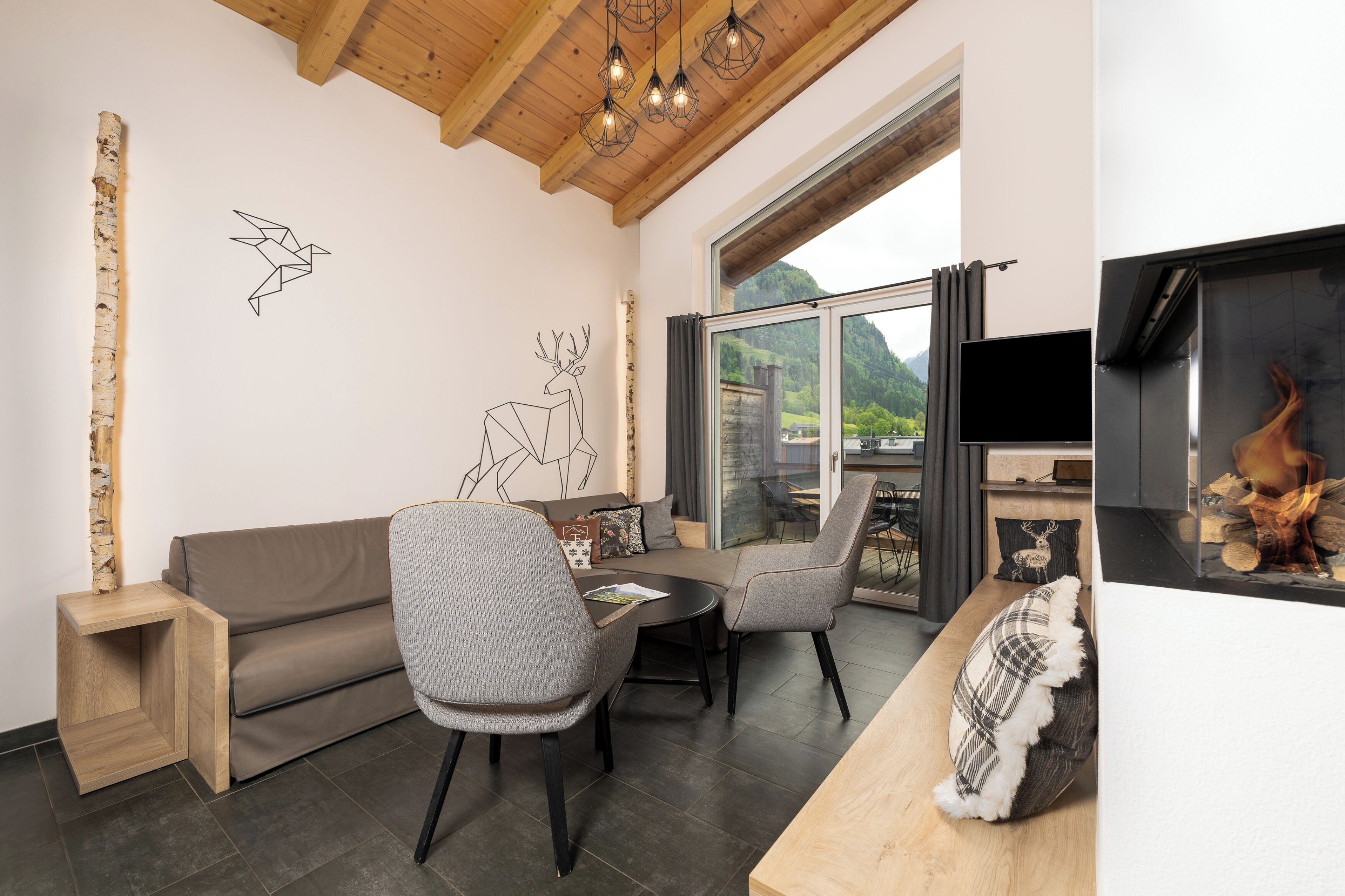 Ein modernes Wohnzimmer mit Holzboden, einer Couch, Sesseln, einem Fernseher und einem Kamin.