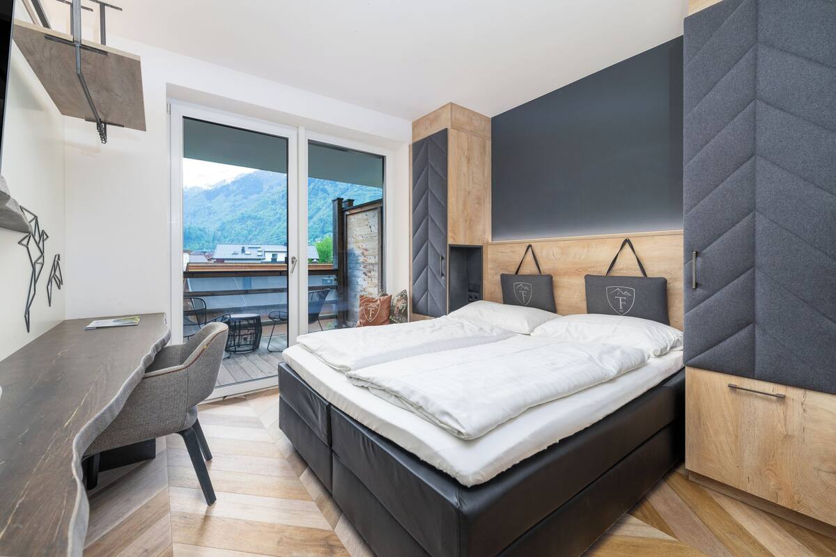 A modern bedroom with a bed, a desk, and a view of mountains.