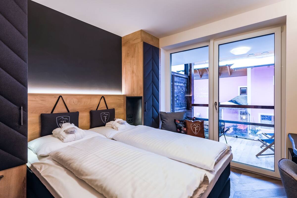 A hotel room with two beds, a dark headboard, a wooden cabinet, and a sliding glass door leading to an outdoor area.