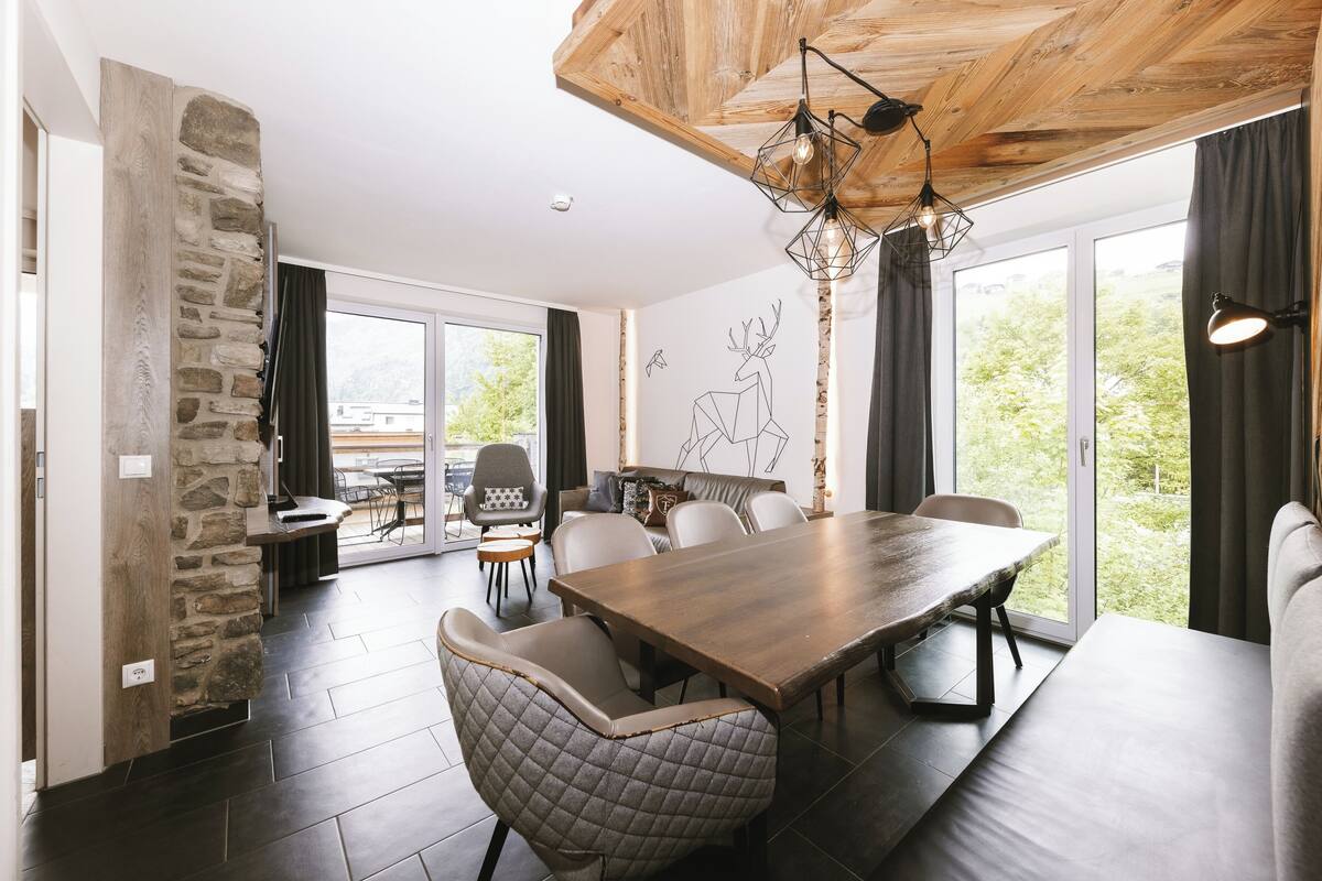 A modern dining area with a large wooden table, cushioned chairs, and a stone accent wall.