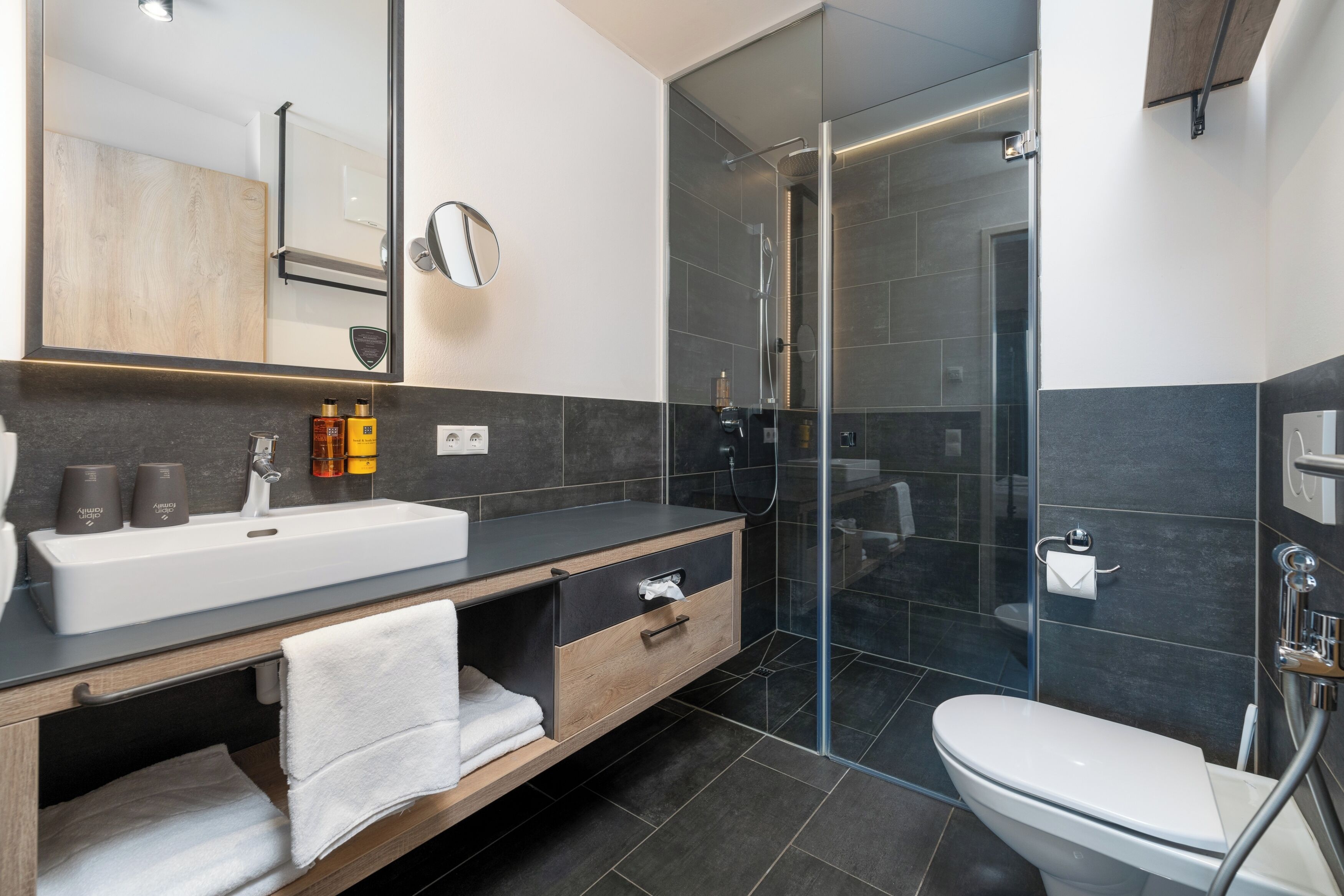 A modern bathroom with a glass-enclosed shower, a white sink, and a wooden vanity.