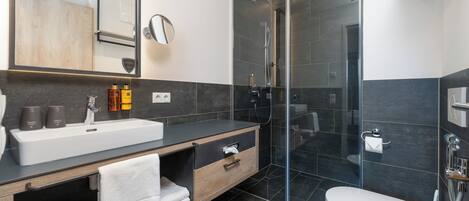 Un baño moderno con ducha envuelta en vidrio, un lavabo blanco y un mueble de tocador de madera.
