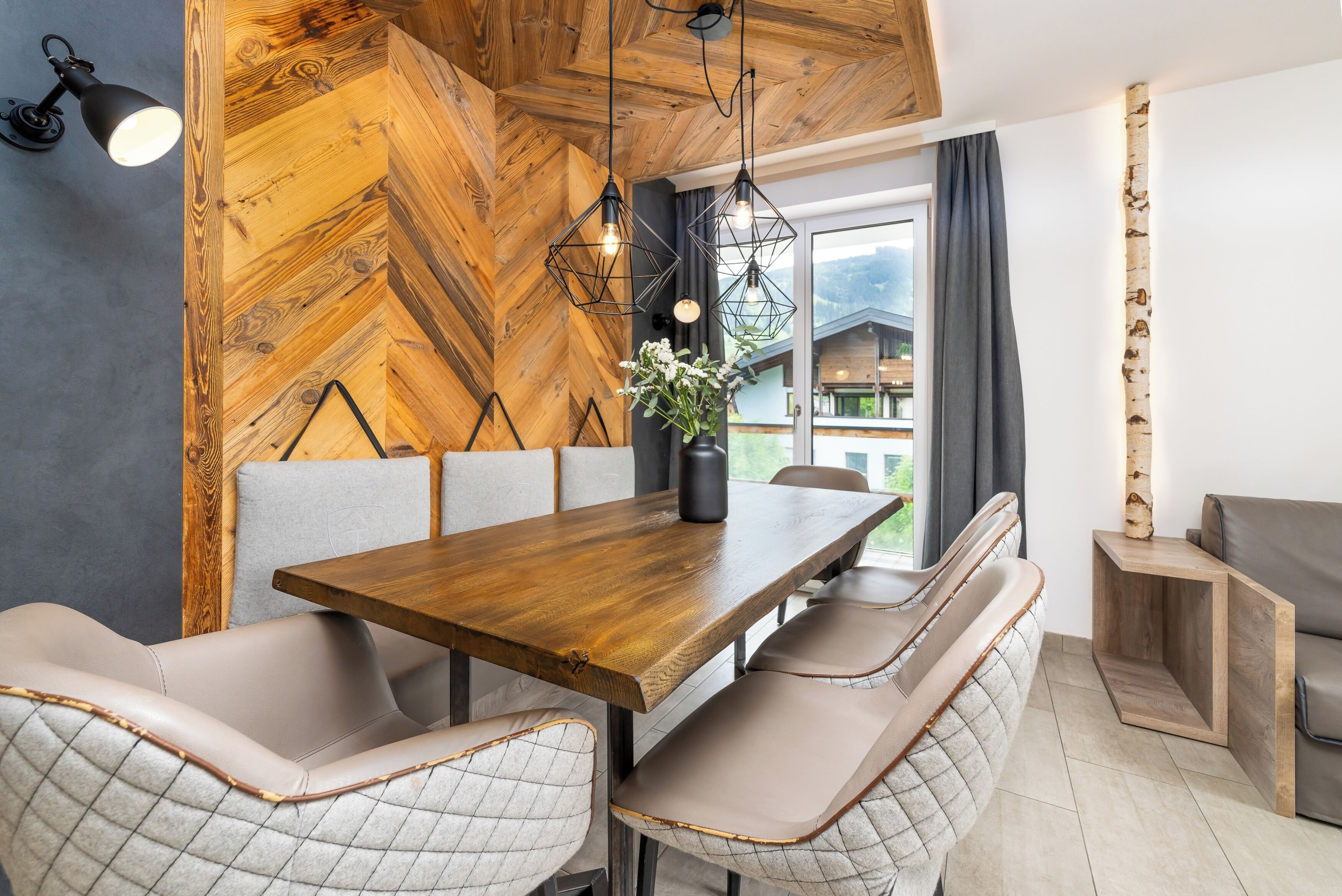 A dining area with a wooden herringbone wall, a wooden table, cushioned benches, and pendant lighting.