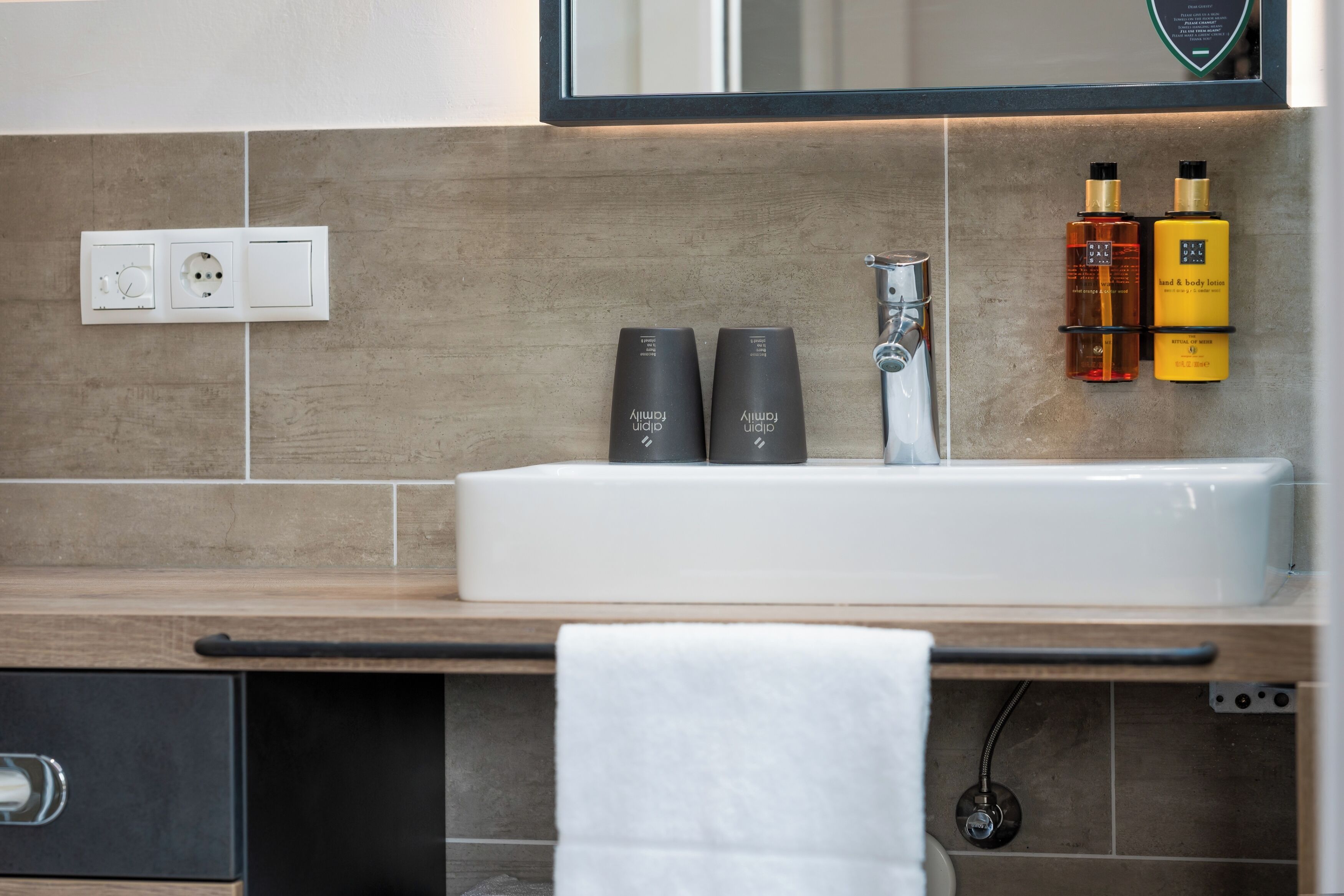 Un baño moderno con un lavabo blanco, dos artículos de tocador negros y dos botellas amarillas de loción corporal y para manos.