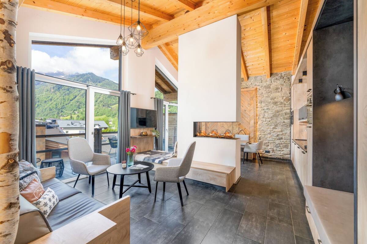 A modern interior with a stone wall, wooden ceiling beams, and a large window overlooking a mountainous landscape.
