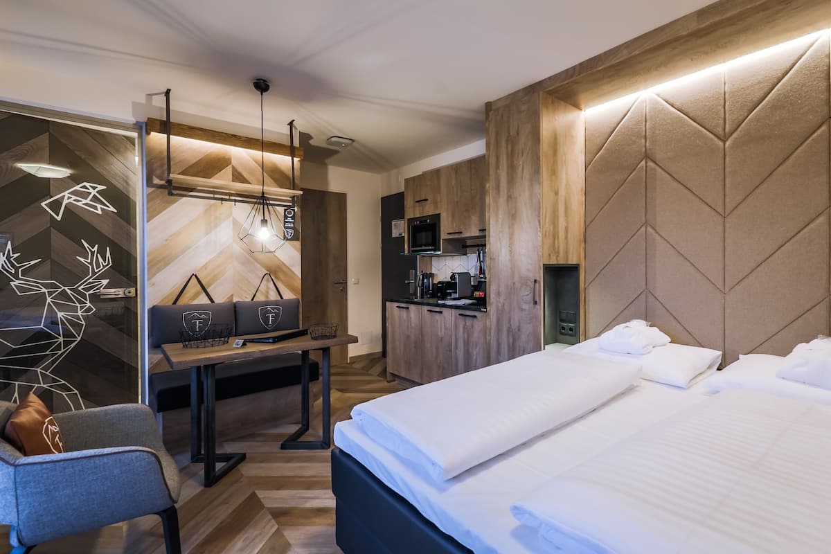 A modern hotel room with a bed, a desk, a kitchenette, and a decorative wall.