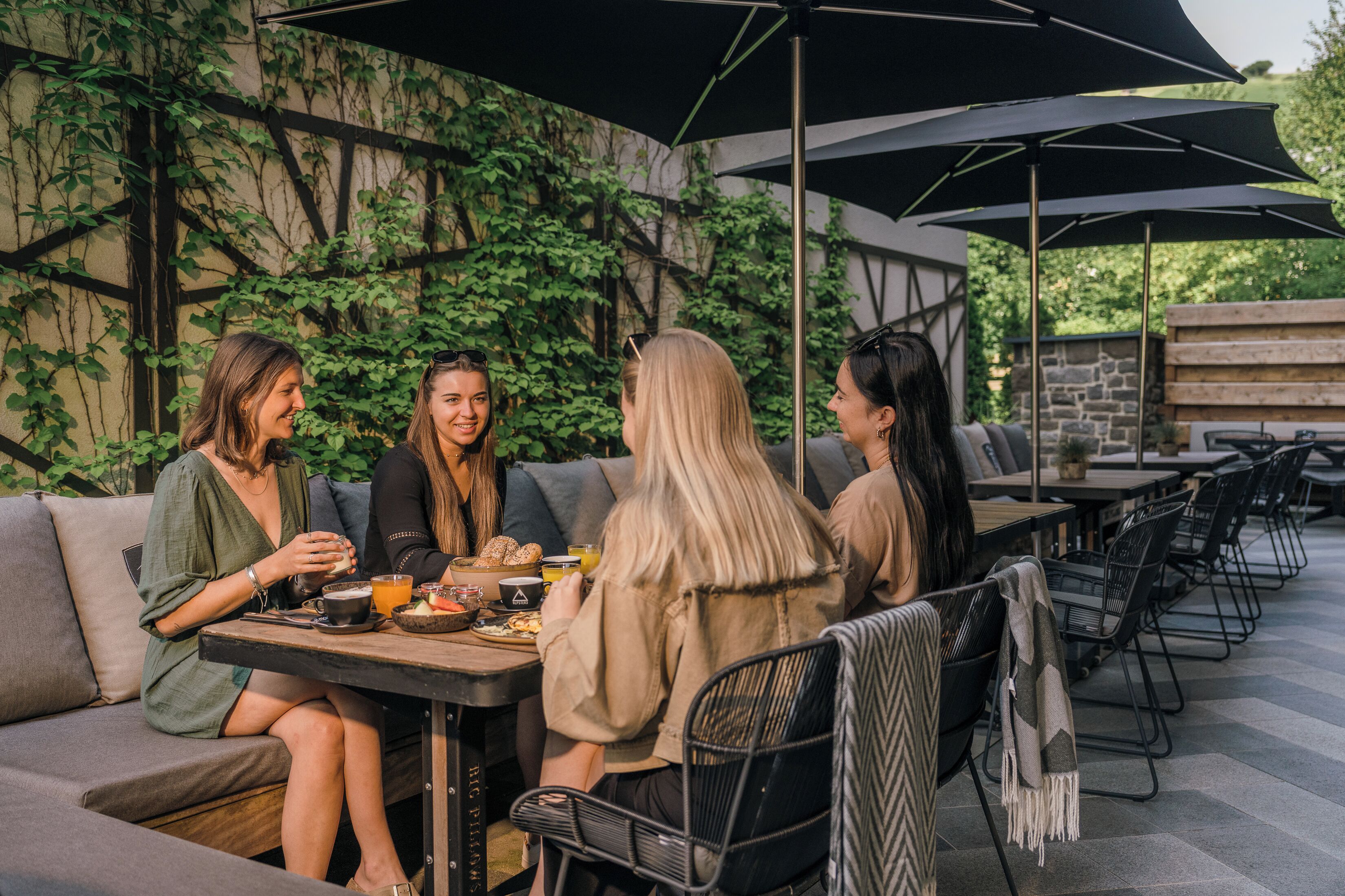 A group of people seated at an outdoor café with tables, chairs, and umbrellas.