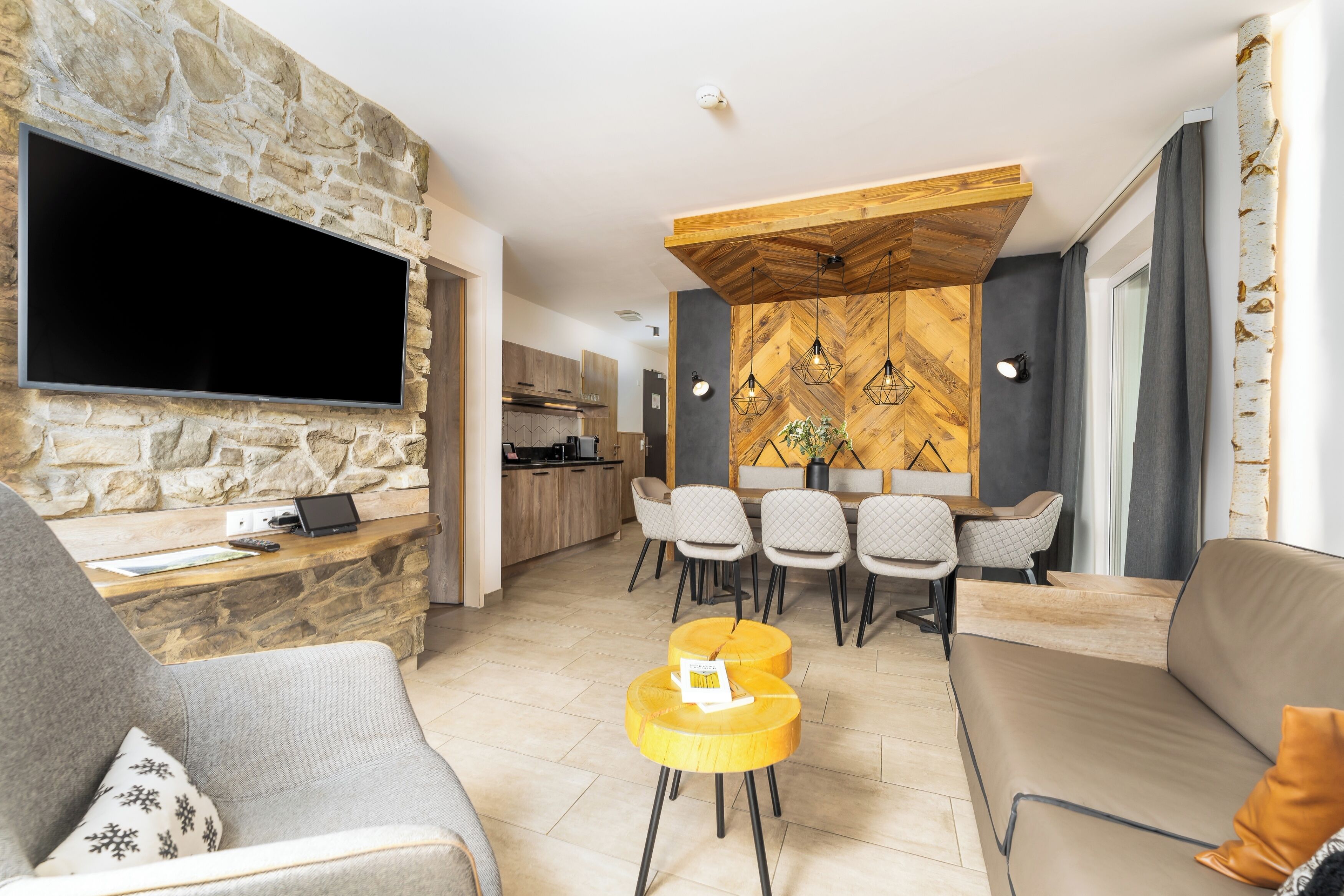 Un soggiorno moderno con parete in pietra, televisore a schermo piatto, soffitto in legno e zona pranzo con sedie e tavolo.
